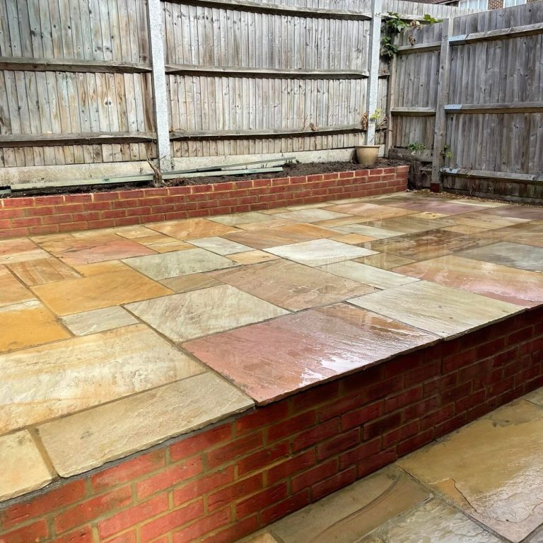 Paved patio area with a brick border and wooden fence in the background.