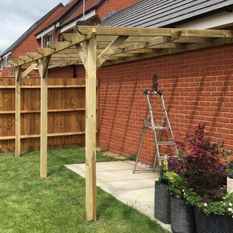 Wooden pergola structure with a ladder, set against a brick wall and garden.